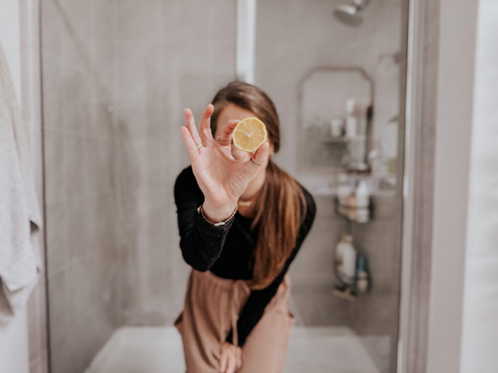 woman holding a lemon in front of a shower with glass shower doors