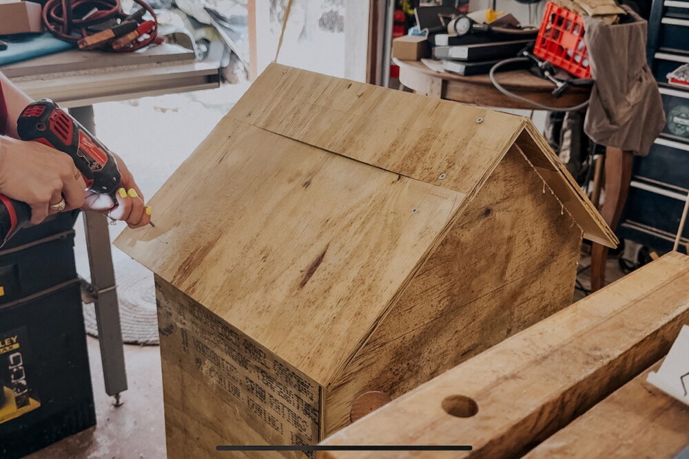Woman's hand drilling on roof pieces for diy Little Free Library