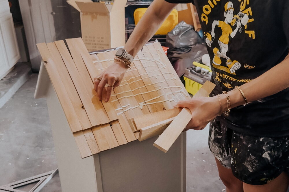 Woman adding cedar shims to a free little library to create a roof