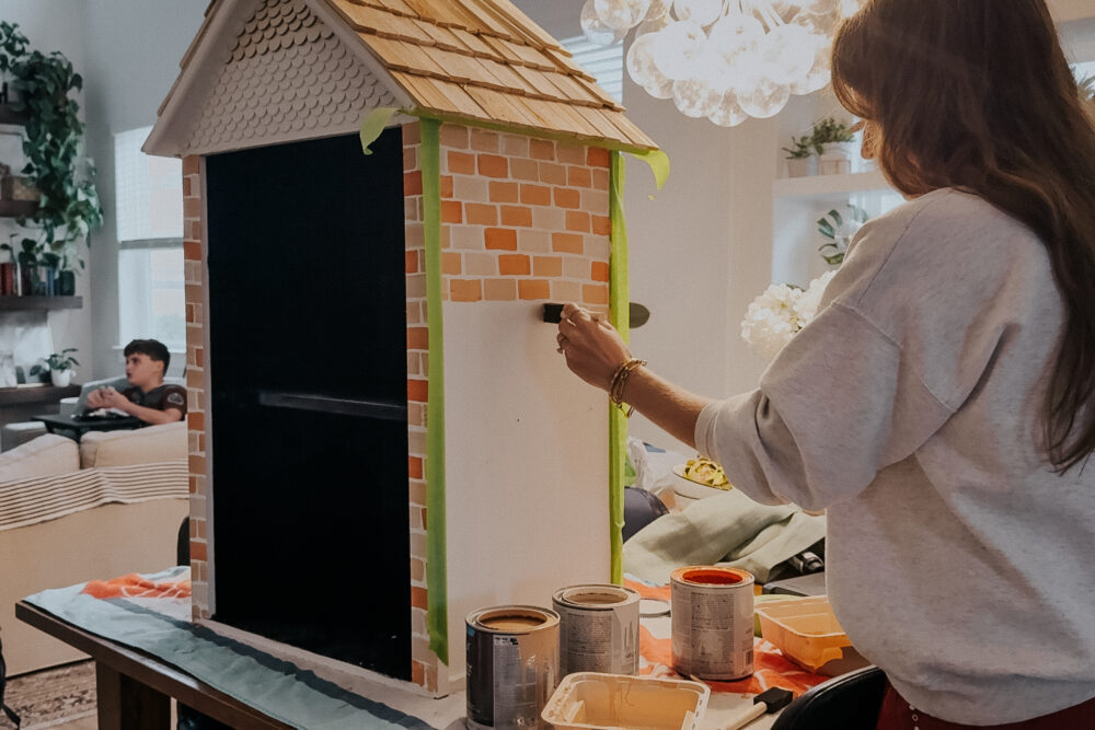 woman painting faux bricks on a Little Free Library 