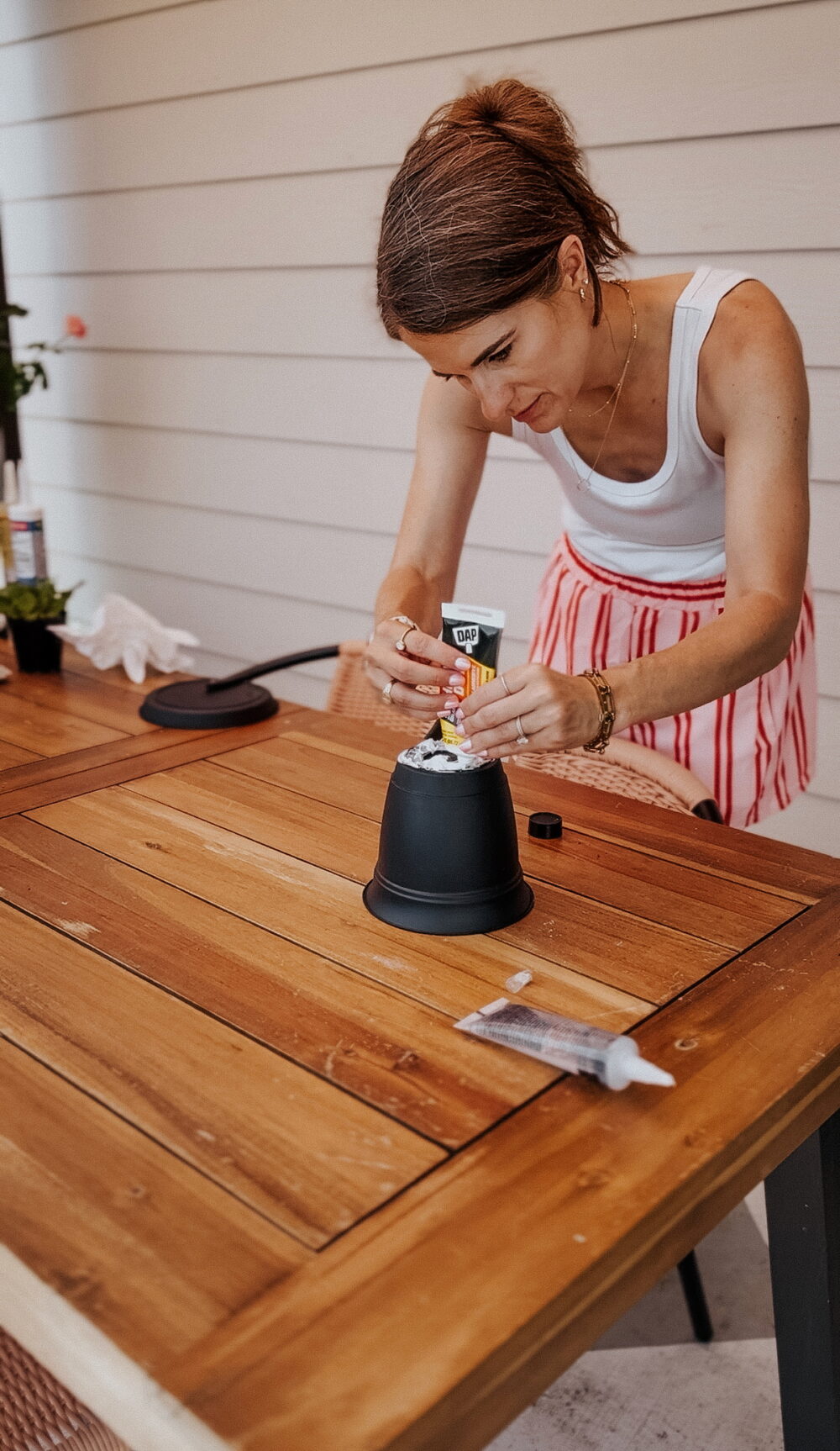 woman using construction adhesive to make a simple plant stand out of a planter