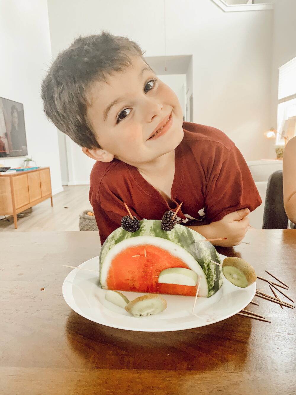 young boy smiling with a fruit dinosaur snack
