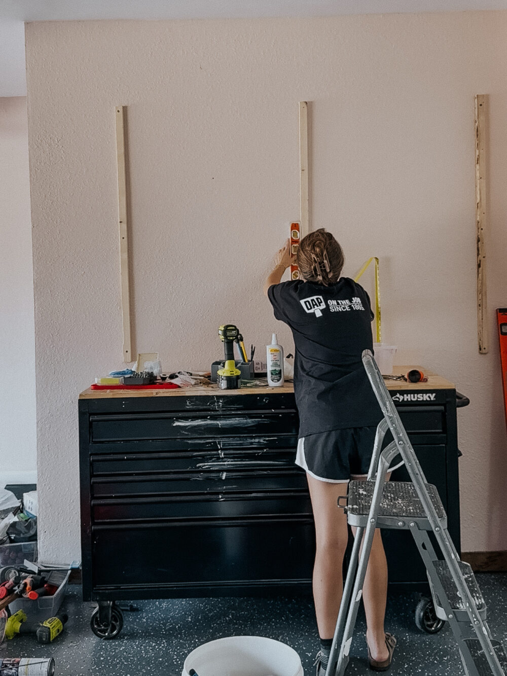 woman hanging furring strips on a wall as a support for a garage pegboard