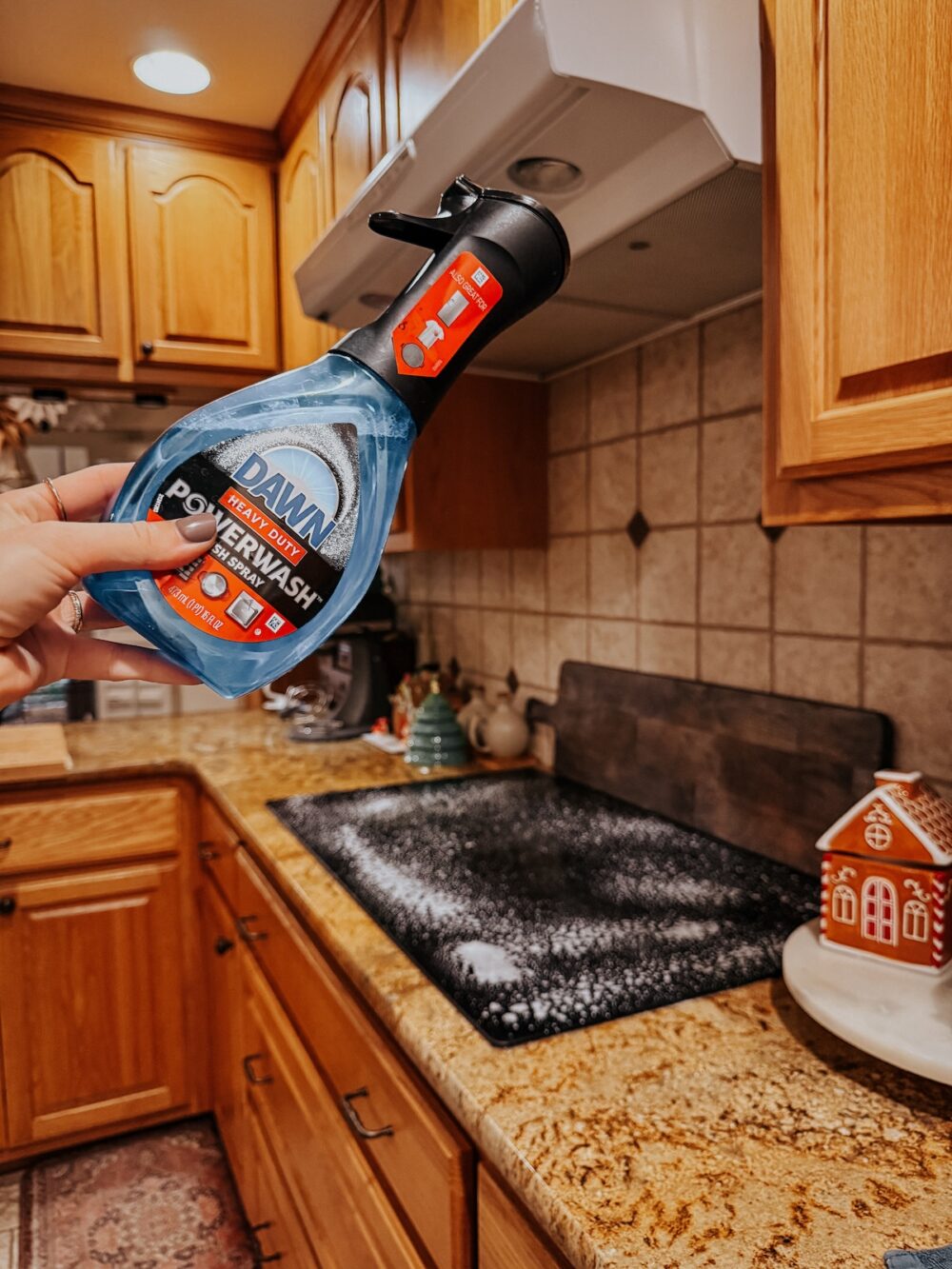 woman's hand holding dawn power wash in front of a glass top stove