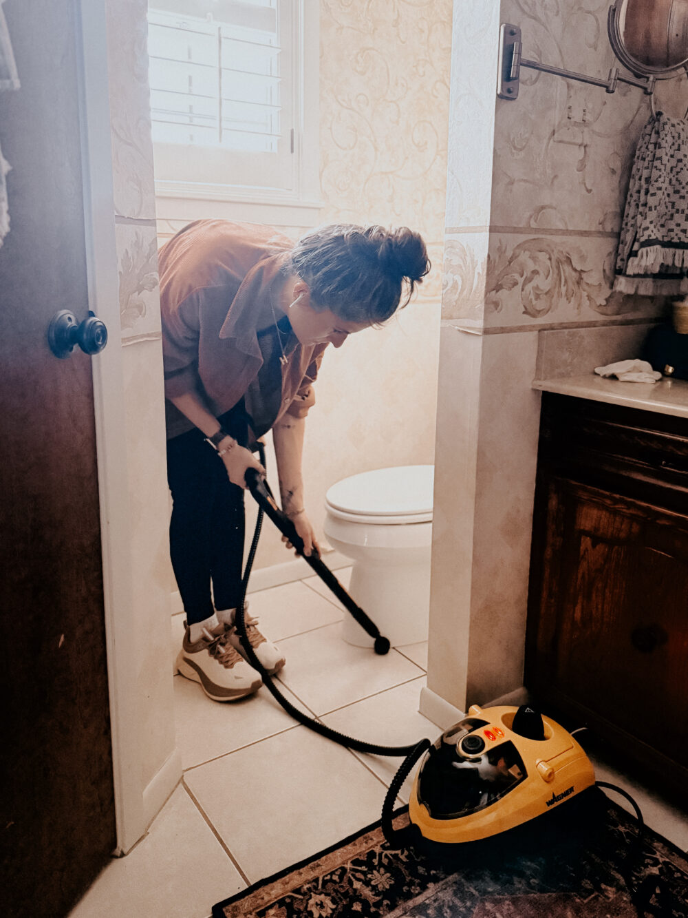 woman cleaning the floor around a toilet using a steam cleaner