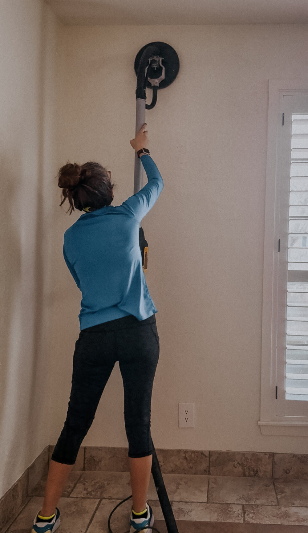 woman using a drywall sander to prep walls for wallpaper