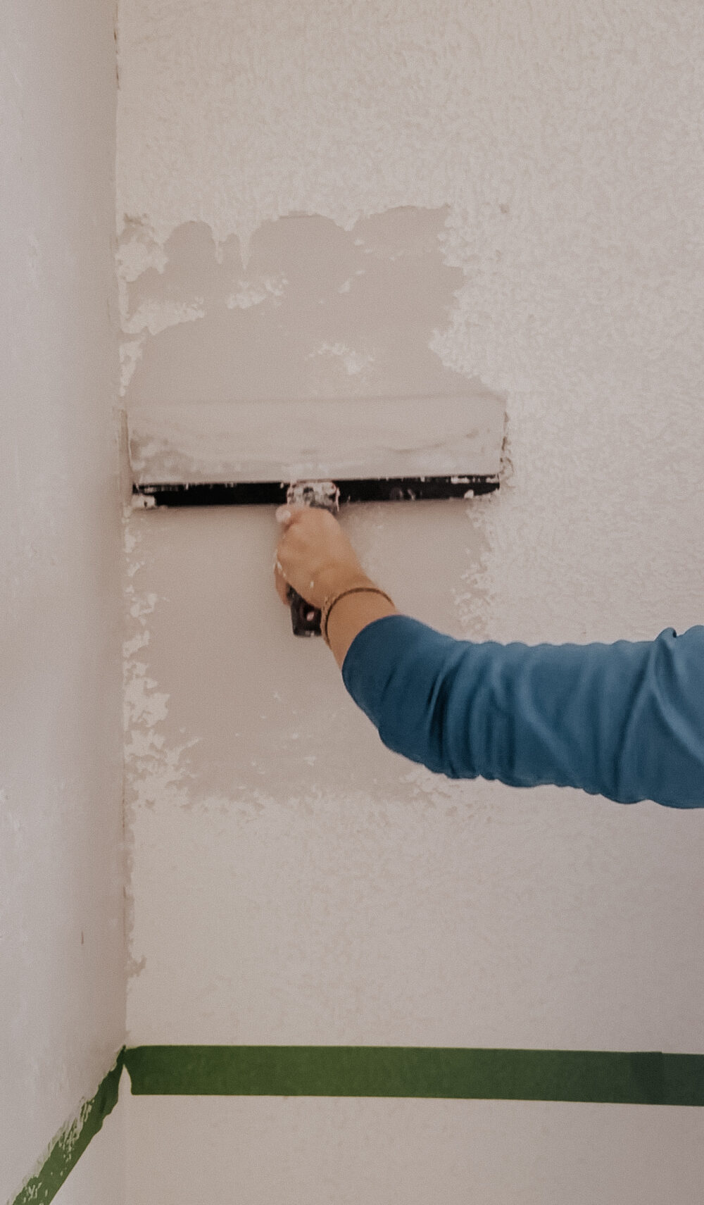 woman's hand adding skim coat to a textured wall