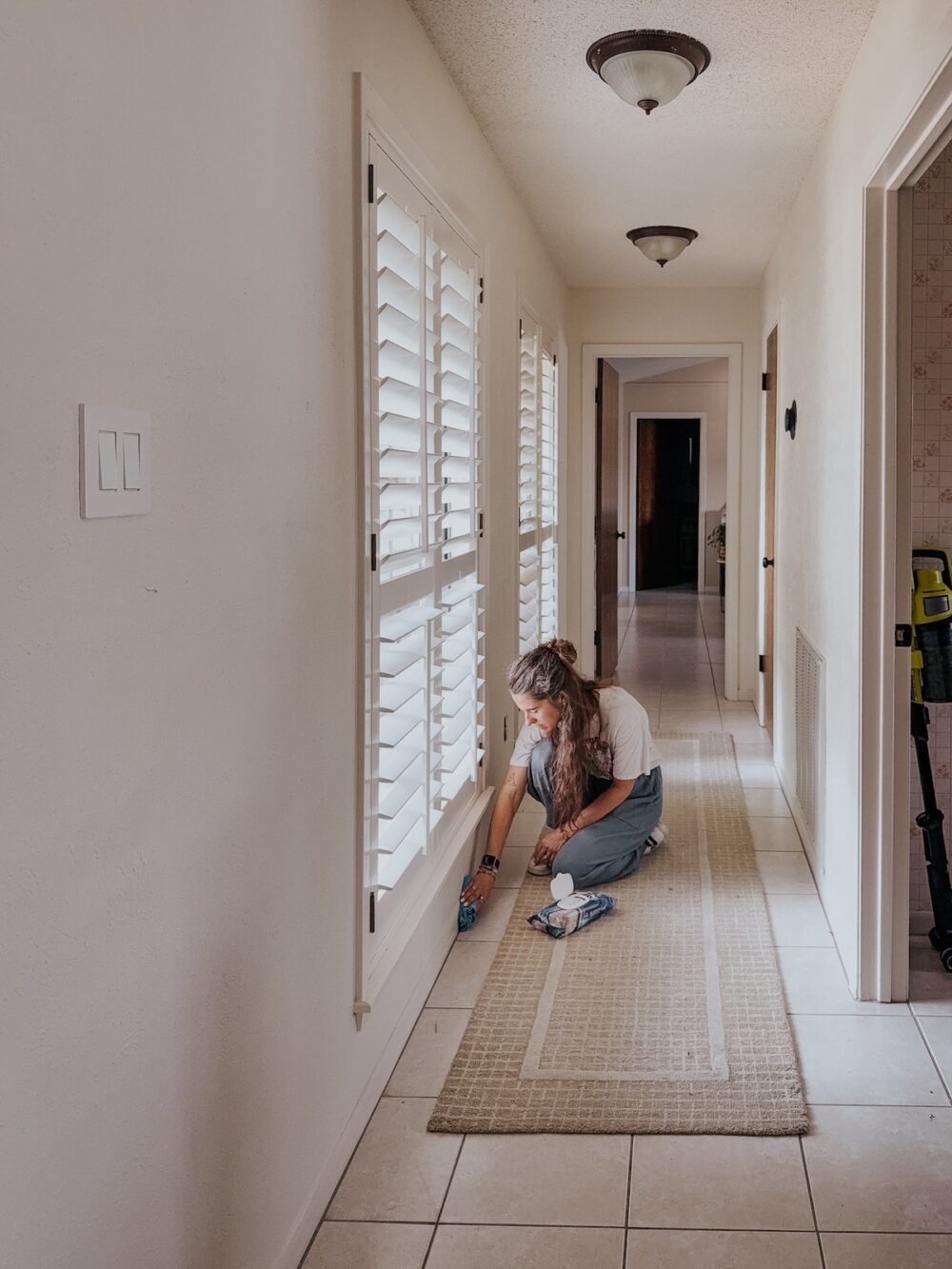 woman cleaning baseboards in a long hallway