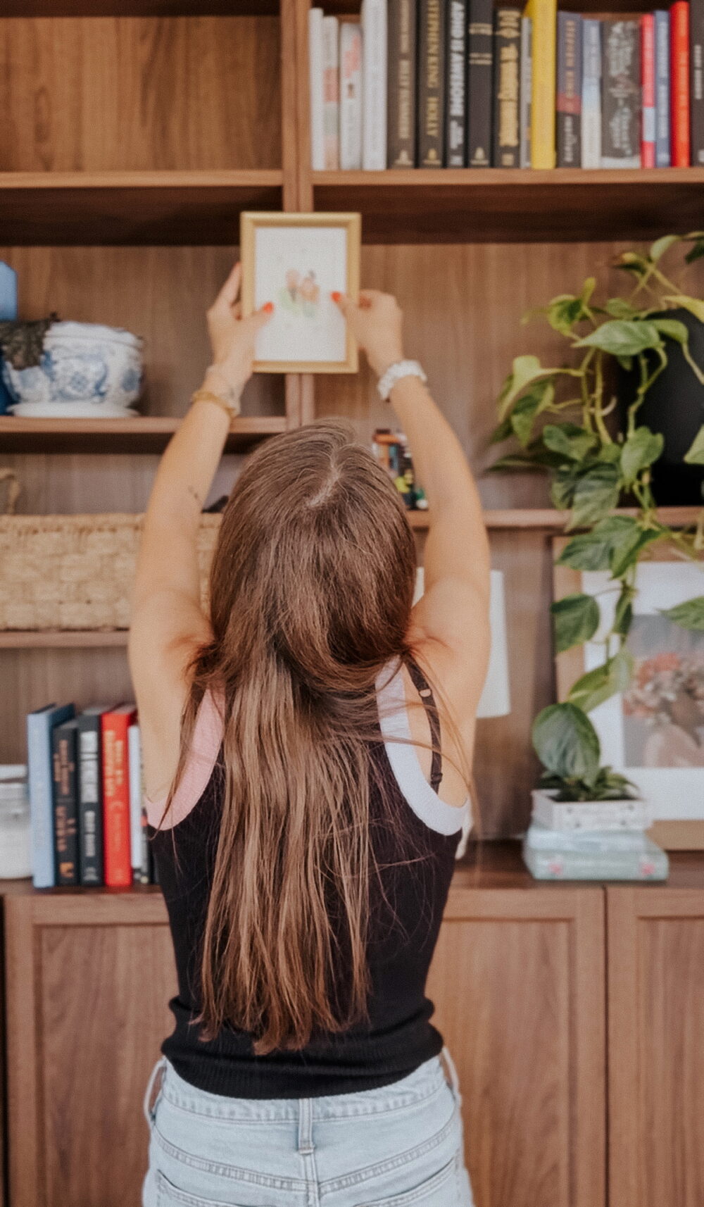 woman hanging art on the front of a bookcase