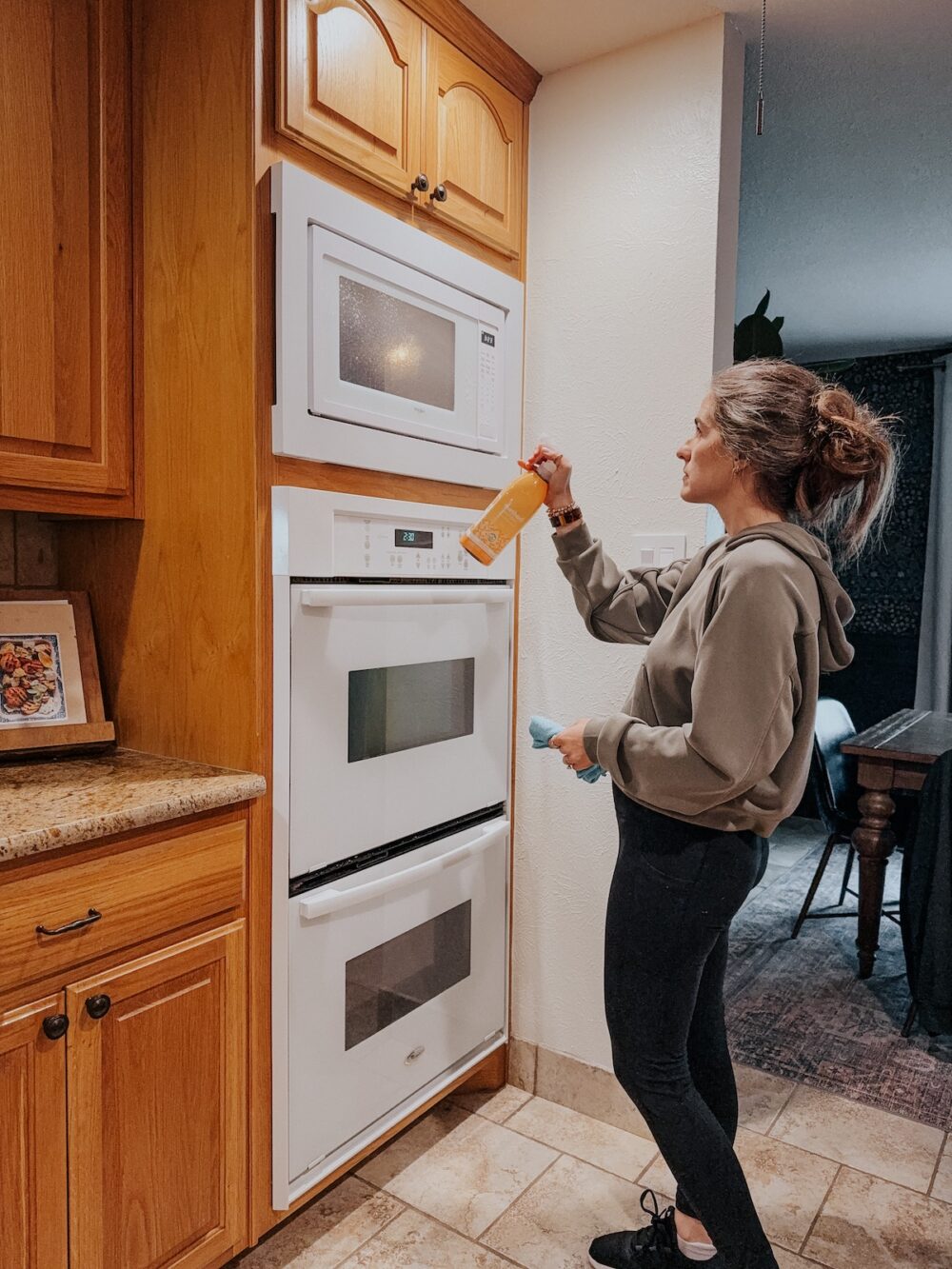 woman using spray and a microfiber cloth to clean the exterior of a microwave