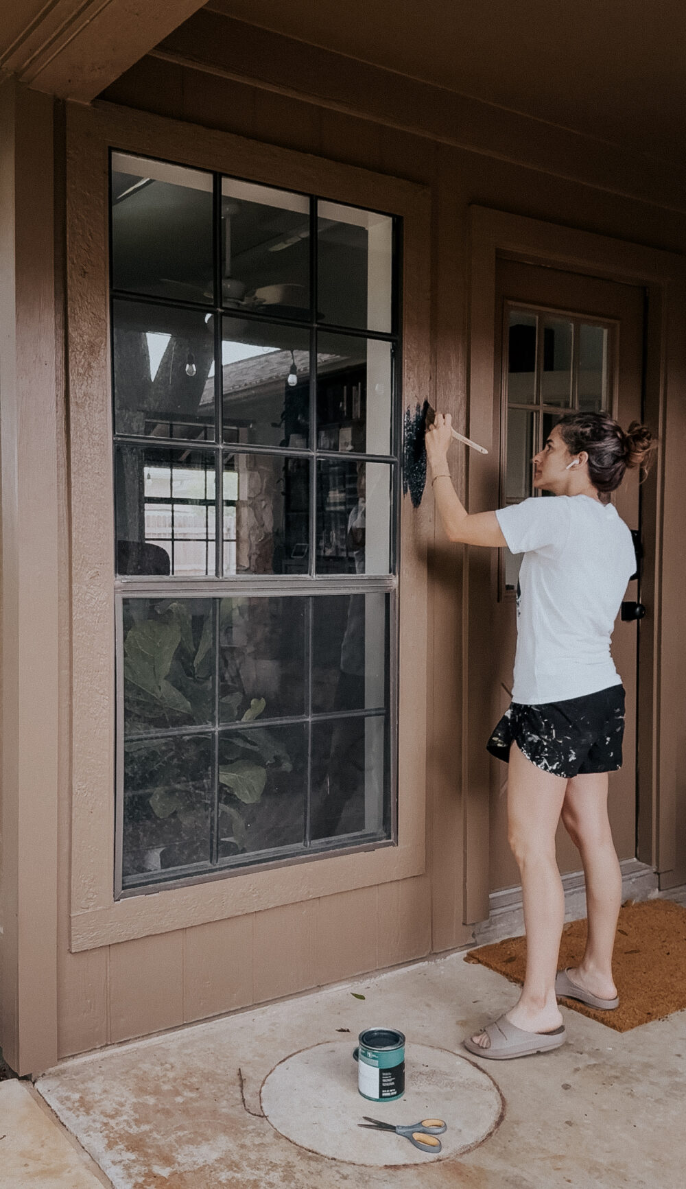 woman painting trim on a house using a painbrush