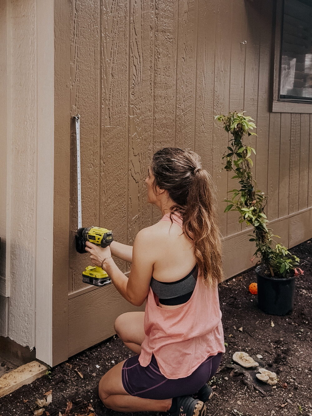 woman measuring an exterior wall to install eye hooks for DIY trellis for trumpet vines