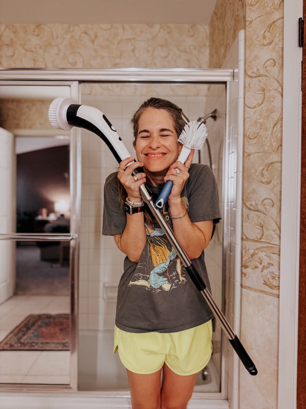 woman smiling and holding a cleaning scrub brush and an electric scrub brush