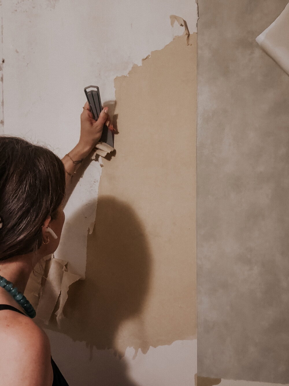 woman scraping wallpaper off a bathroom wall