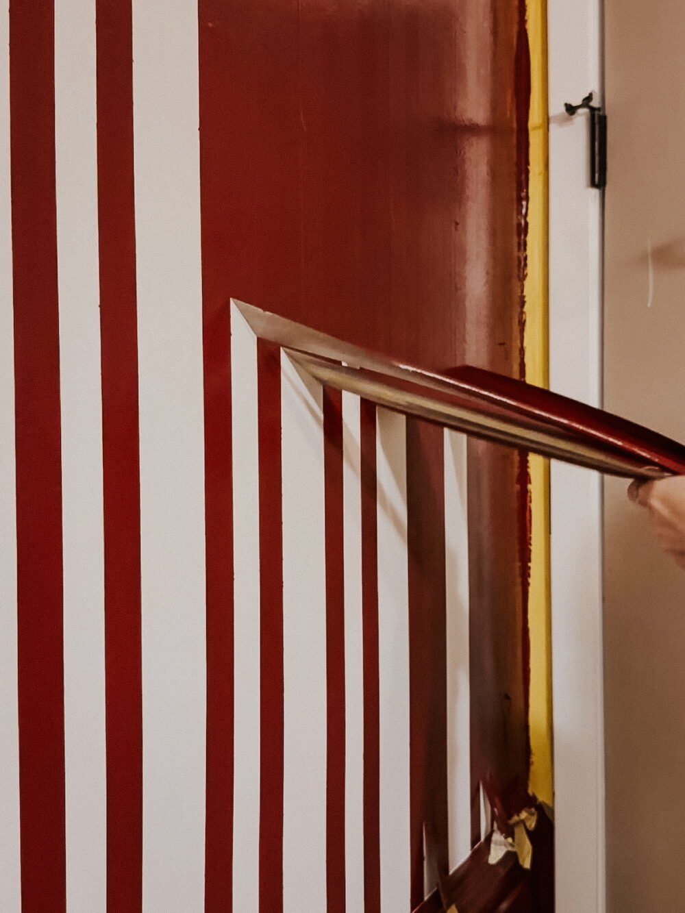 Painted stripes on a wall with a woman's hand removing tape