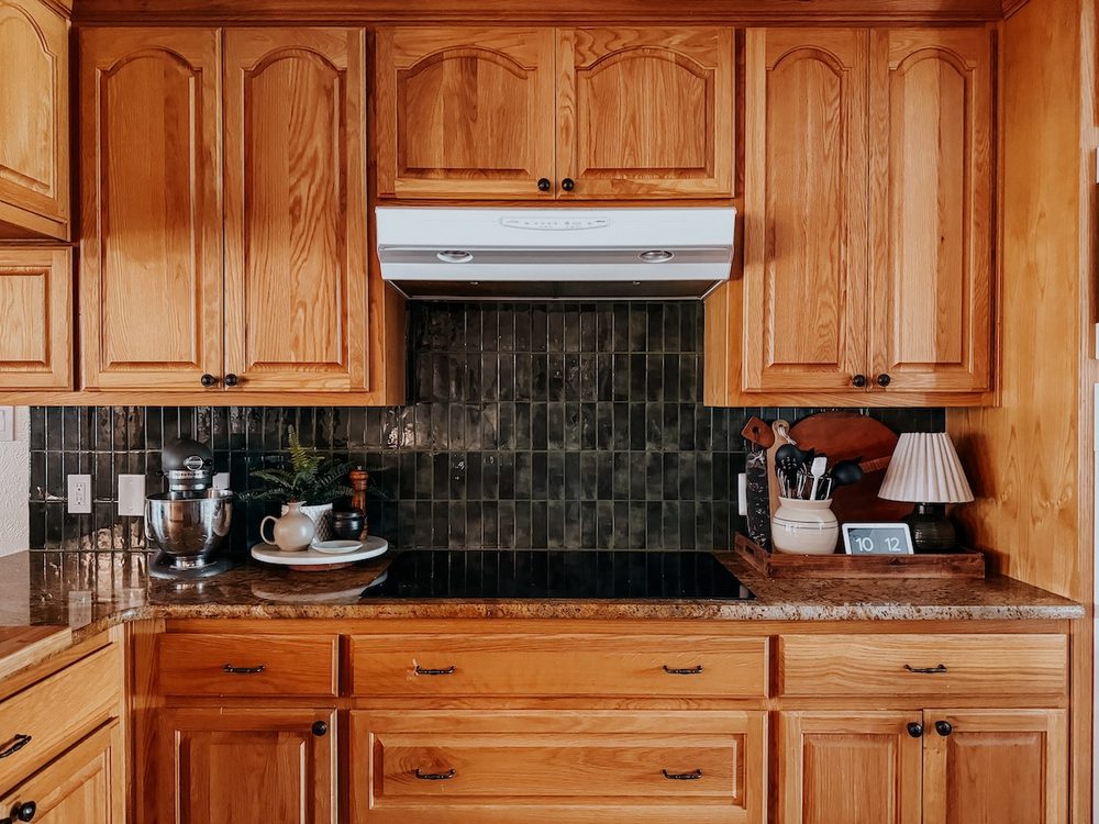 a kitchen with honey oak cabinets and green peel and stick backsplash tiles